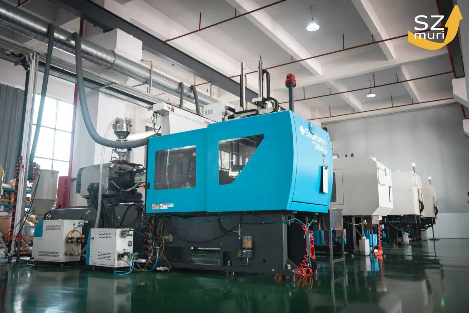 Eine blaue Spritzgussmaschine steht in einer modernen, hellen Fabrikhalle