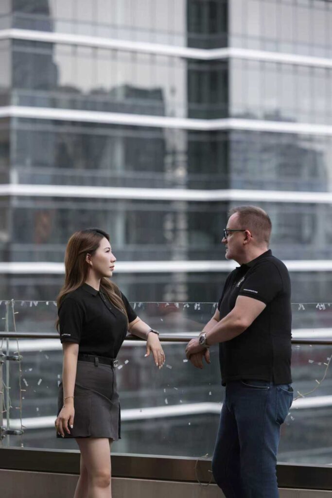Zwei Personen im Gespräch auf einer Terrasse vor einem modernen Glasgebäude